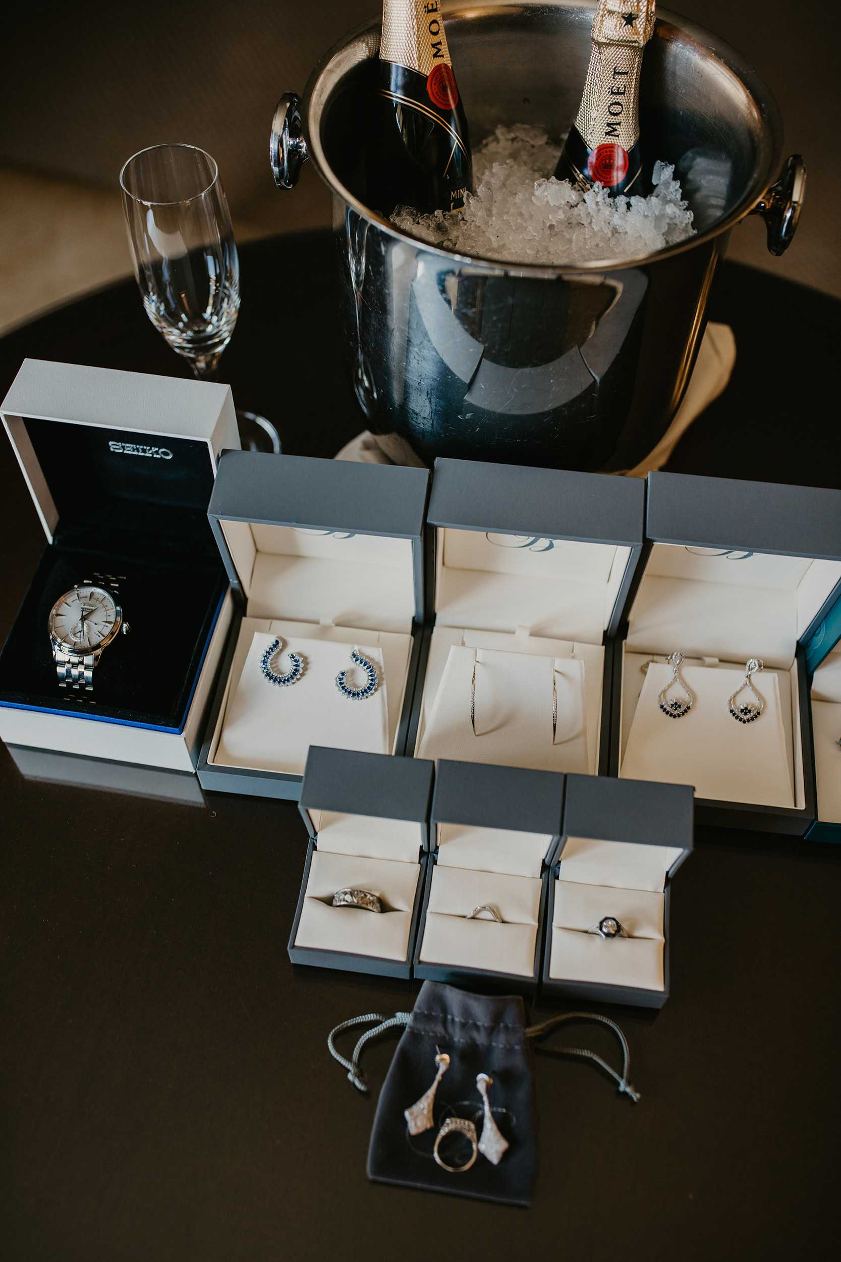A row of Bulow boxes with sapphire earrings, bands and a watch beside champagne on ice